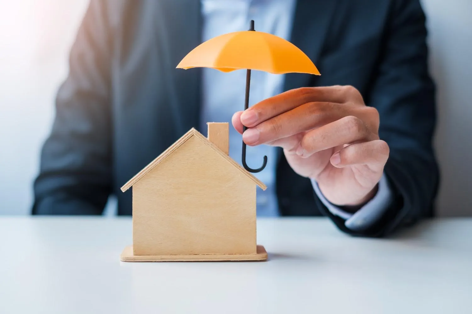 Small wooden house sheltered under an umbrella, representing home insurance