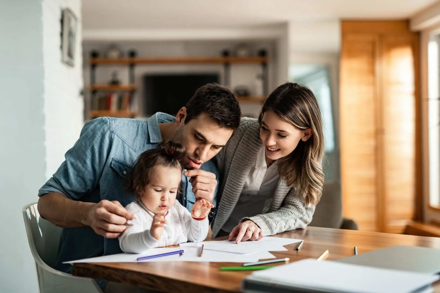 Parents and their young child drawing together at the kitchen table